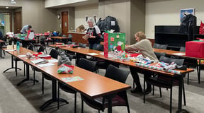 Associates gather in meeting room to help wrap presents for families in need.